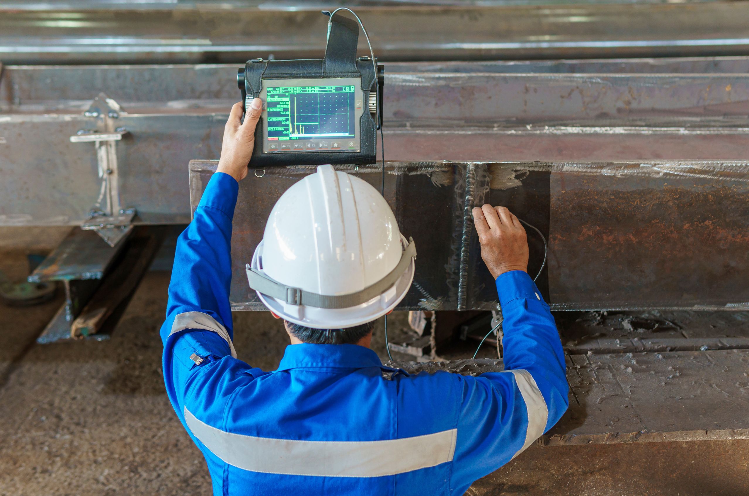 Engineer in a hard hat uses a device to inspect a metal beam with precision.