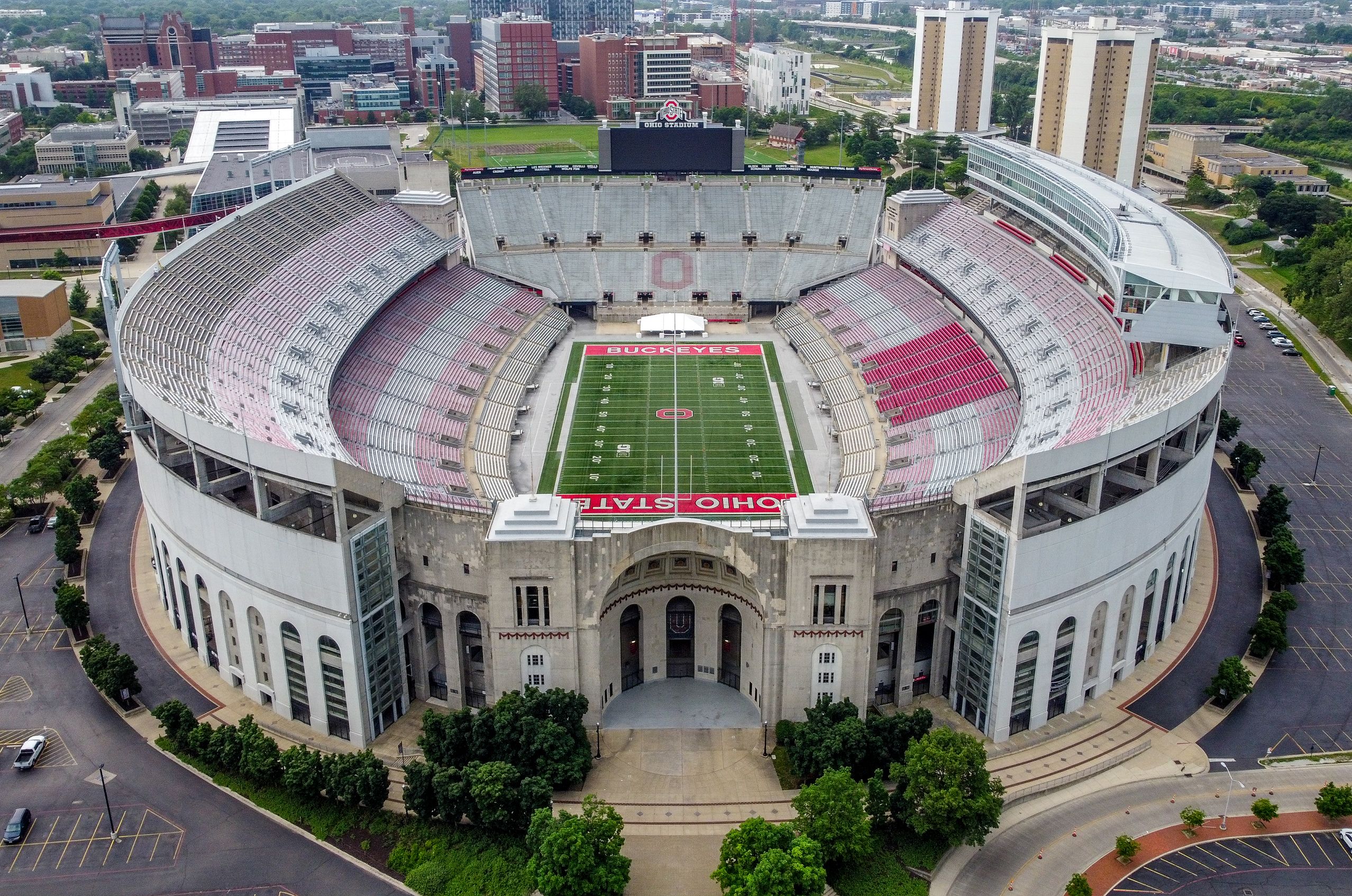 Aerial view of Ohio Stadium, surrounded by the Columbus, OH cityscape of buildings and trees.