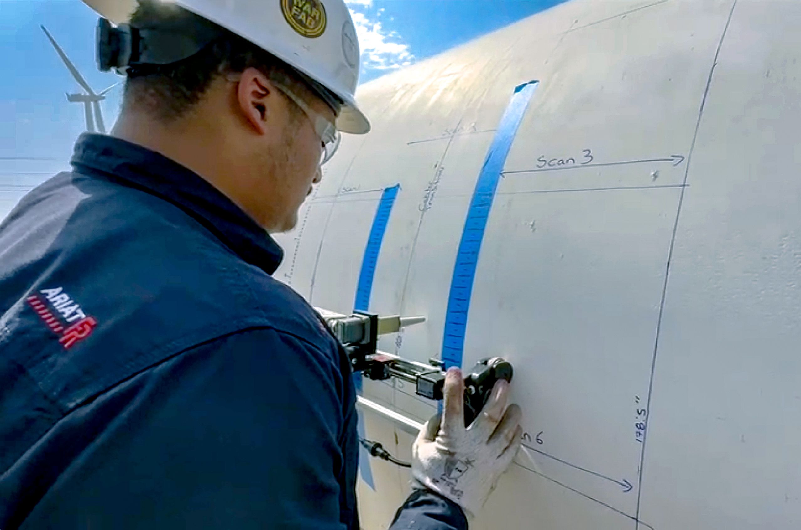 Worker in safety gear inspects a wind turbine blade with measuring tools and markings, under a clear blue sky.