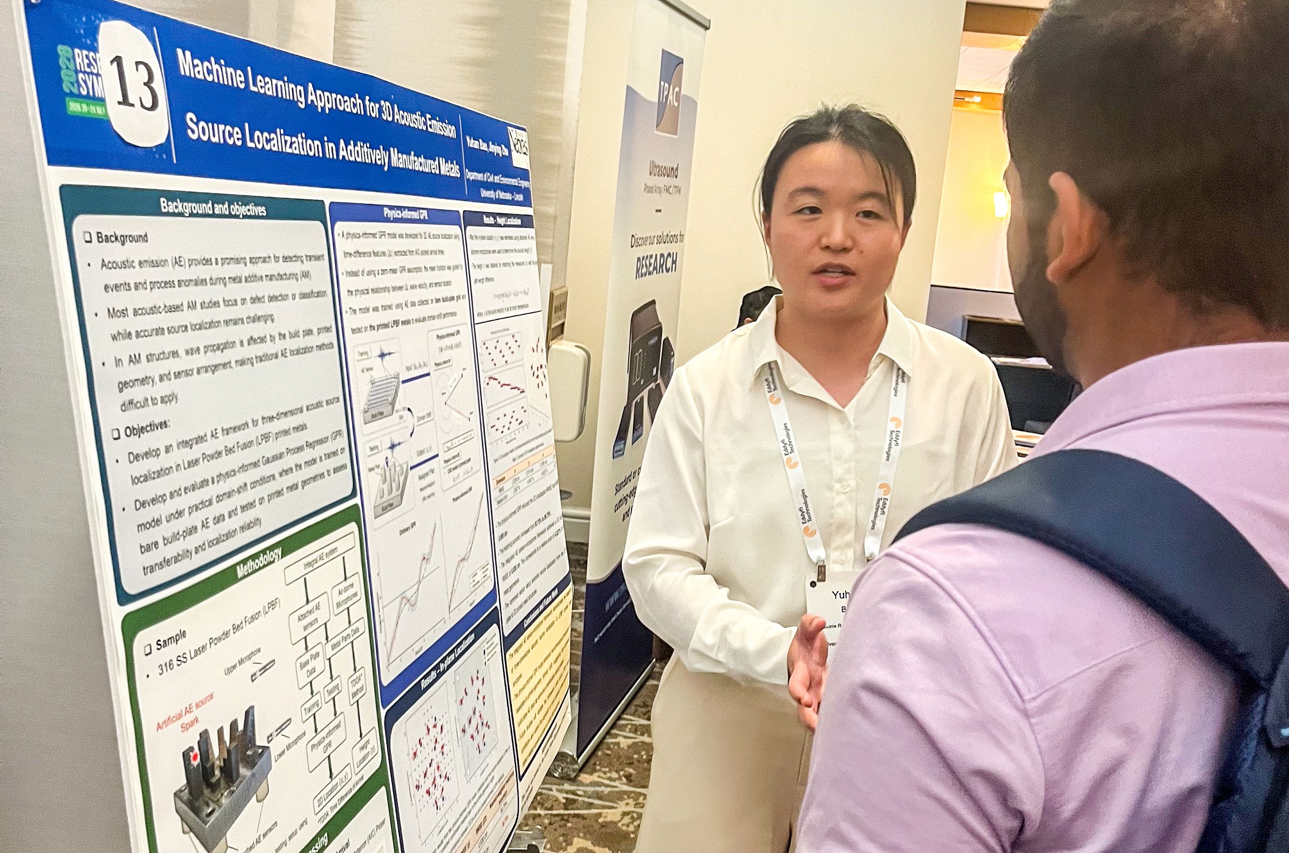 A person presents a poster on machine learning for 3D acoustic emission at a conference, discussing with an attendee.