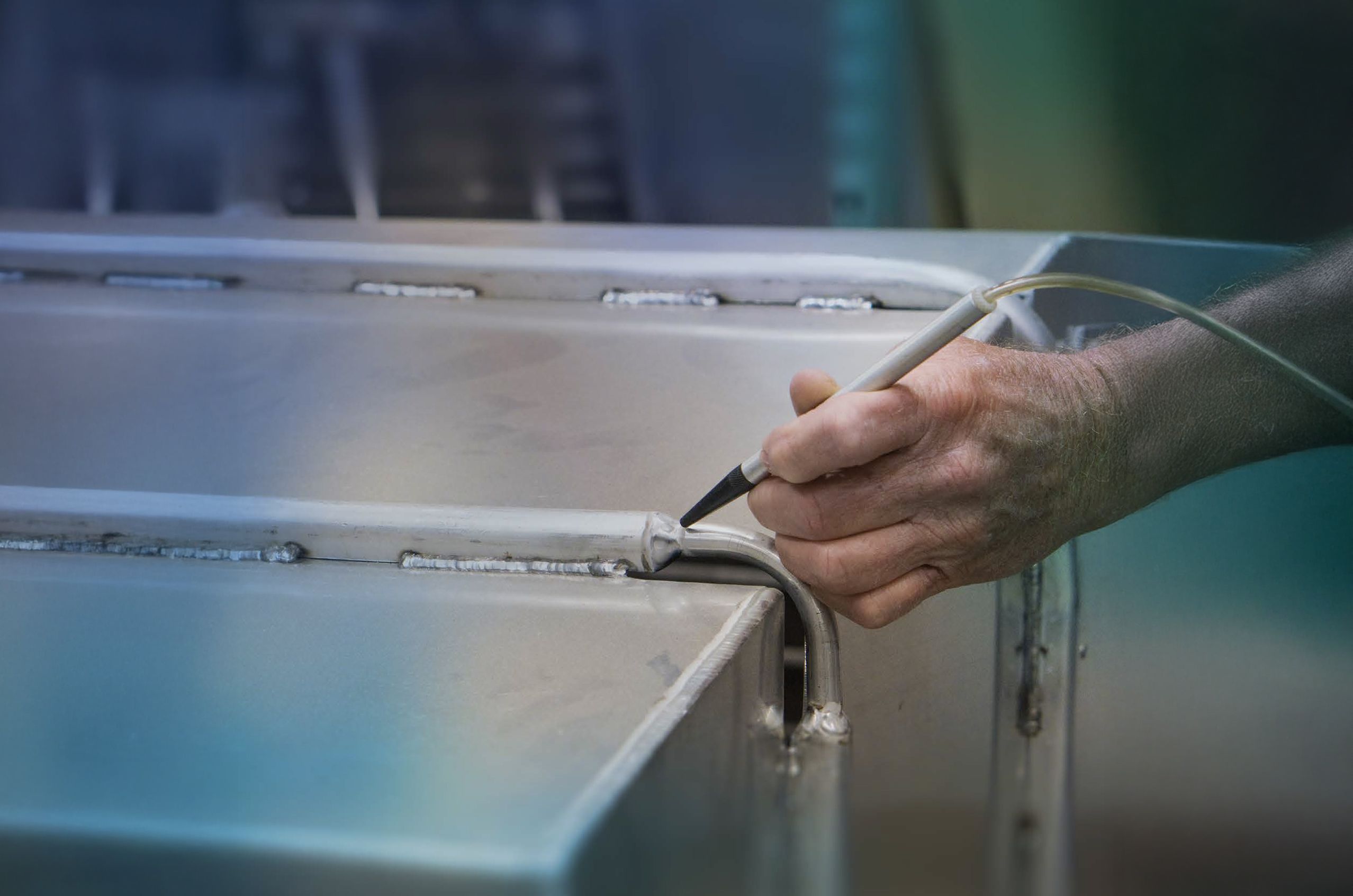 A person using a handheld device to inspect welds on a metal surface.