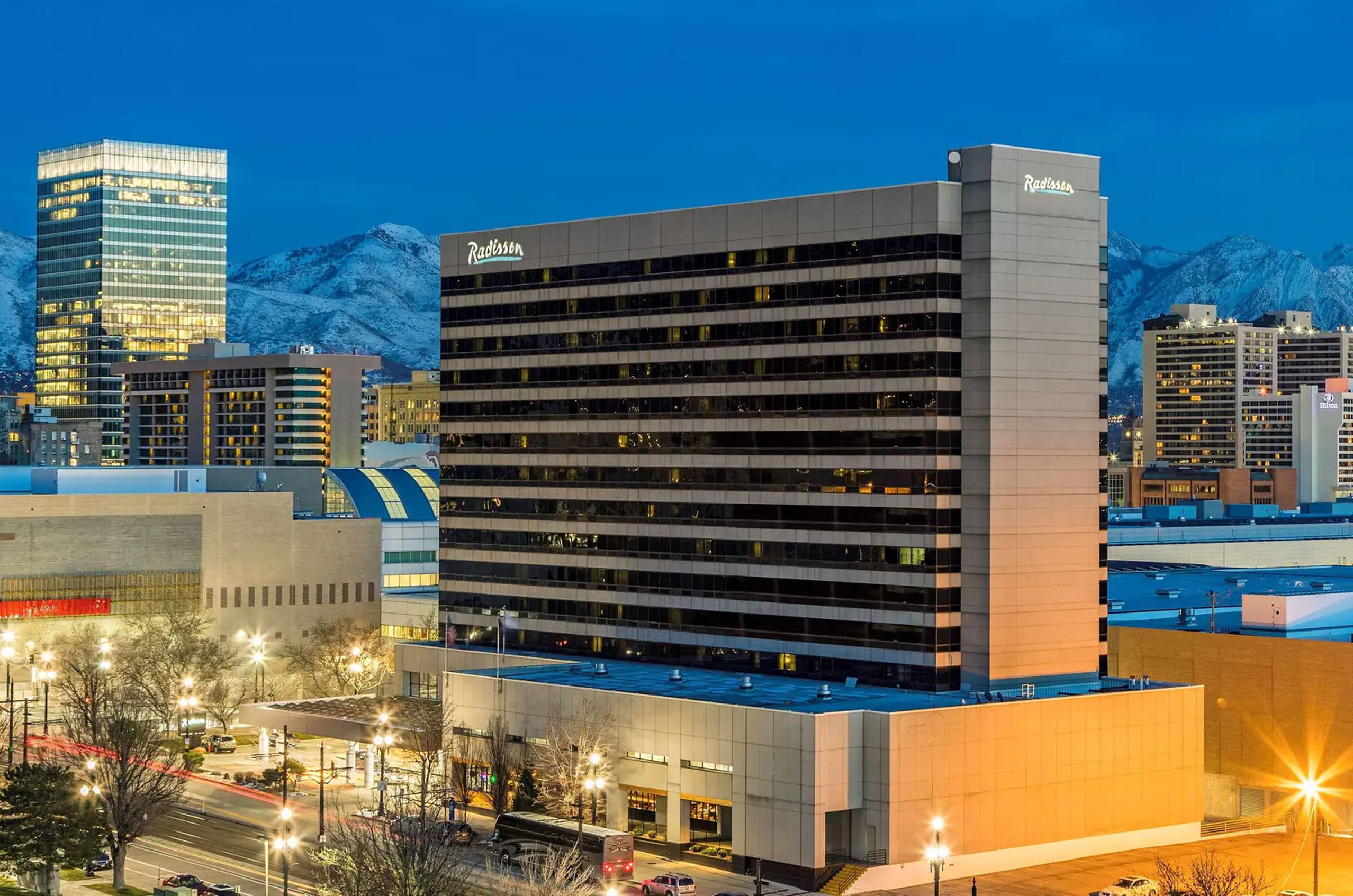 A tall hotel building at night, with city lights and mountains in the background under a clear blue sky.