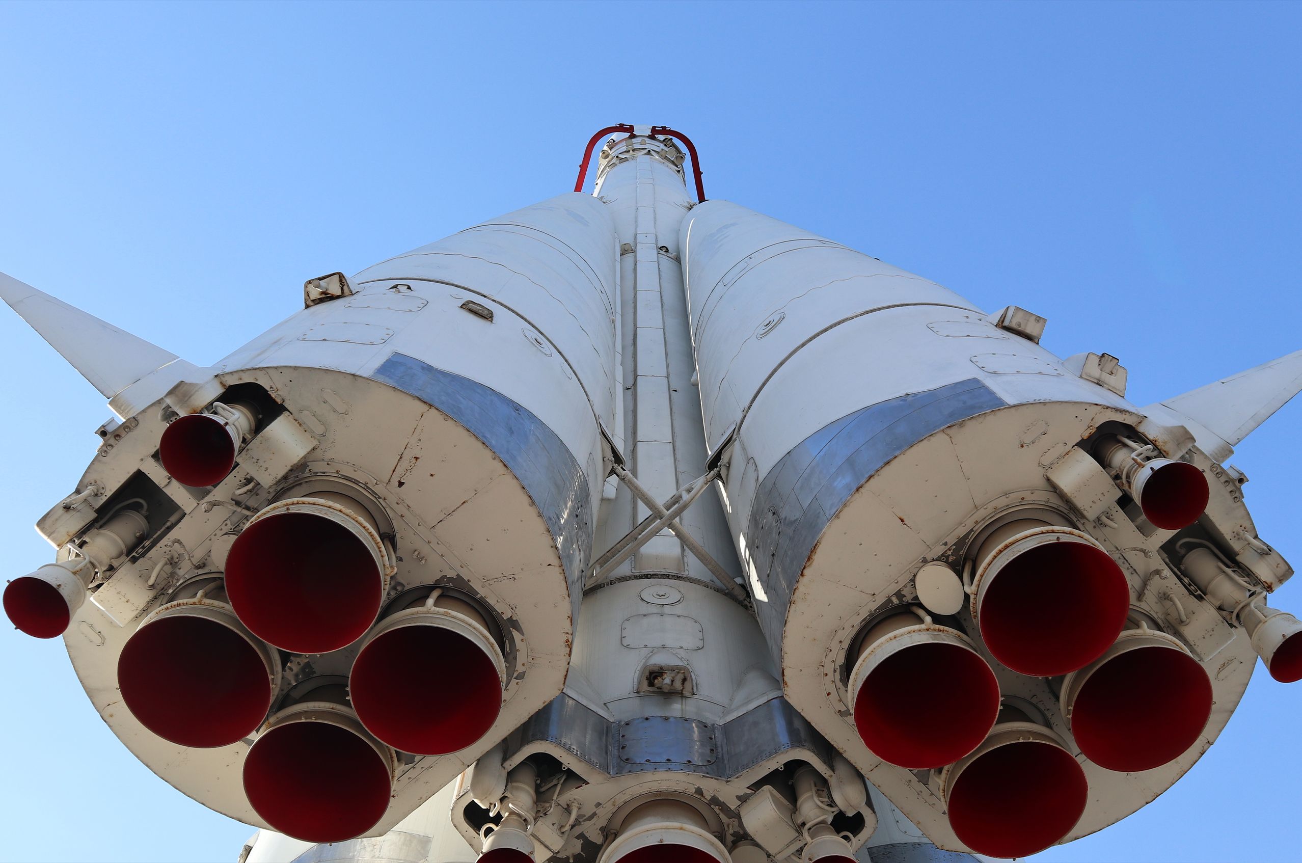 Close-up view of the underside of a white rocket with multiple red nozzles against a clear blue sky.
