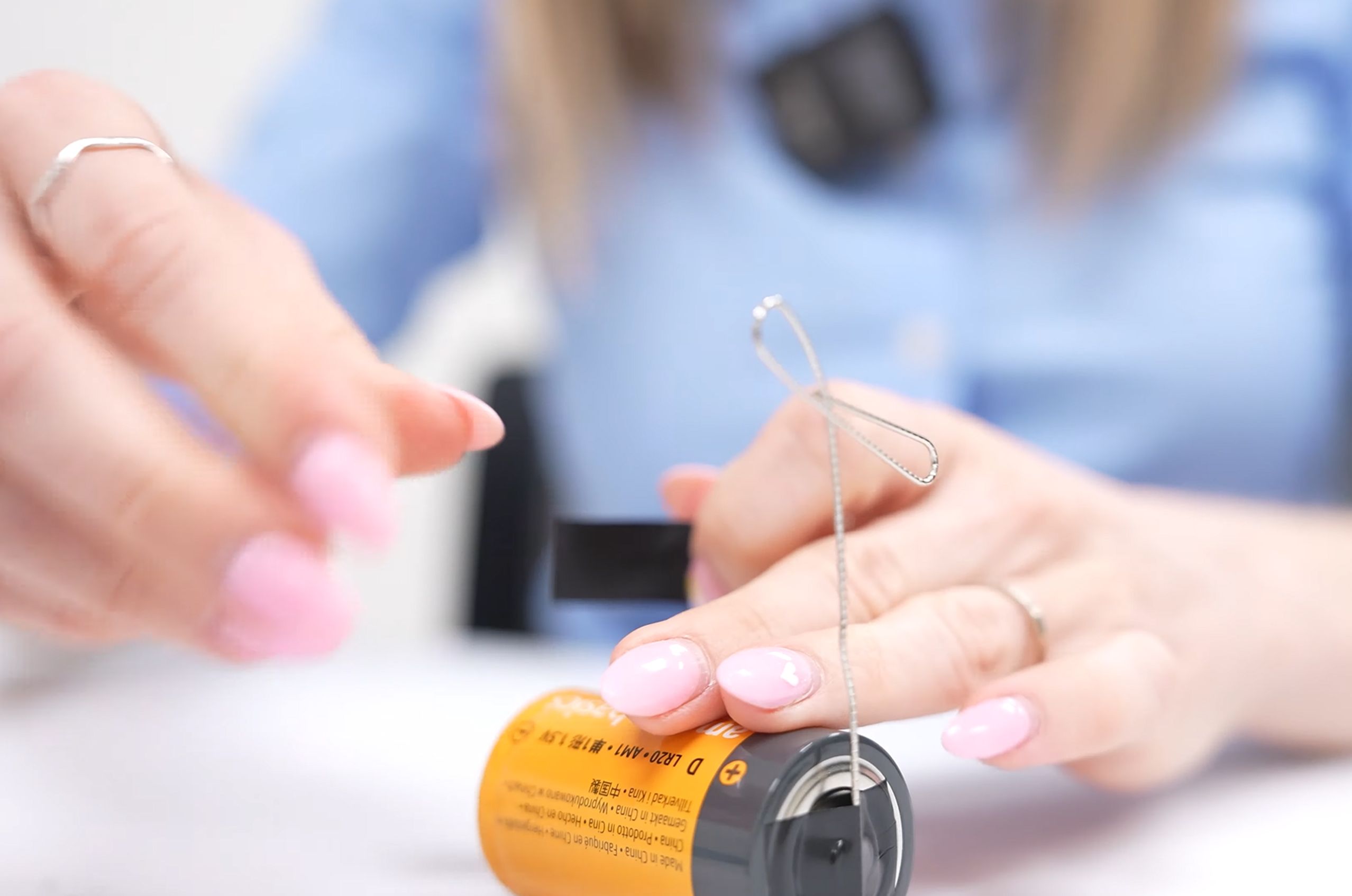 Person demonstrating how to attach a paperclip to a battery.