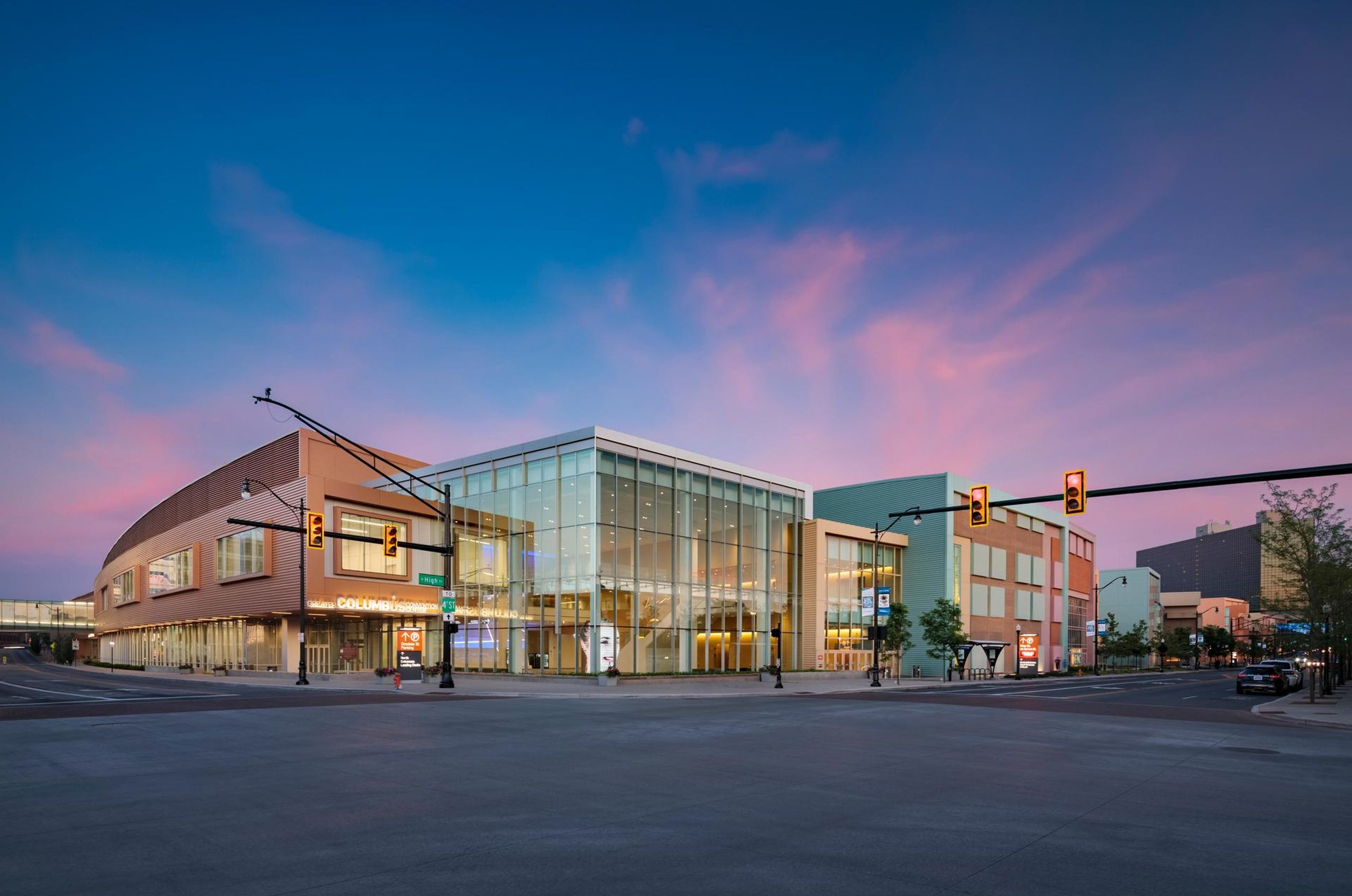 Greater Columbus Convention Center (GCCC) with glass facade at a street intersection during sunset, featuring a clear sky with pink clouds and traffic lights.