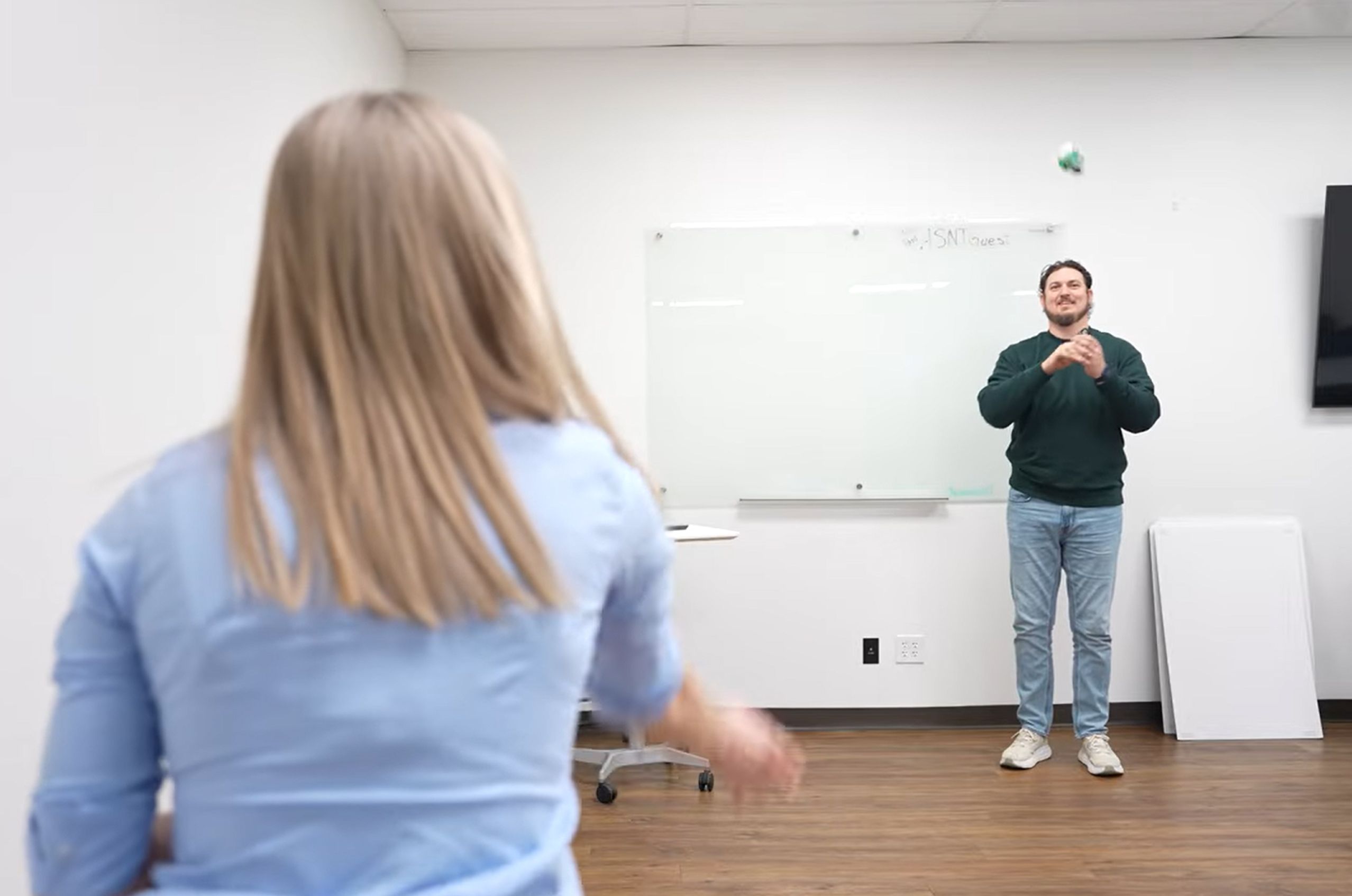Two people  play catch with a small ball. One person is throwing, while the other prepares to catch.