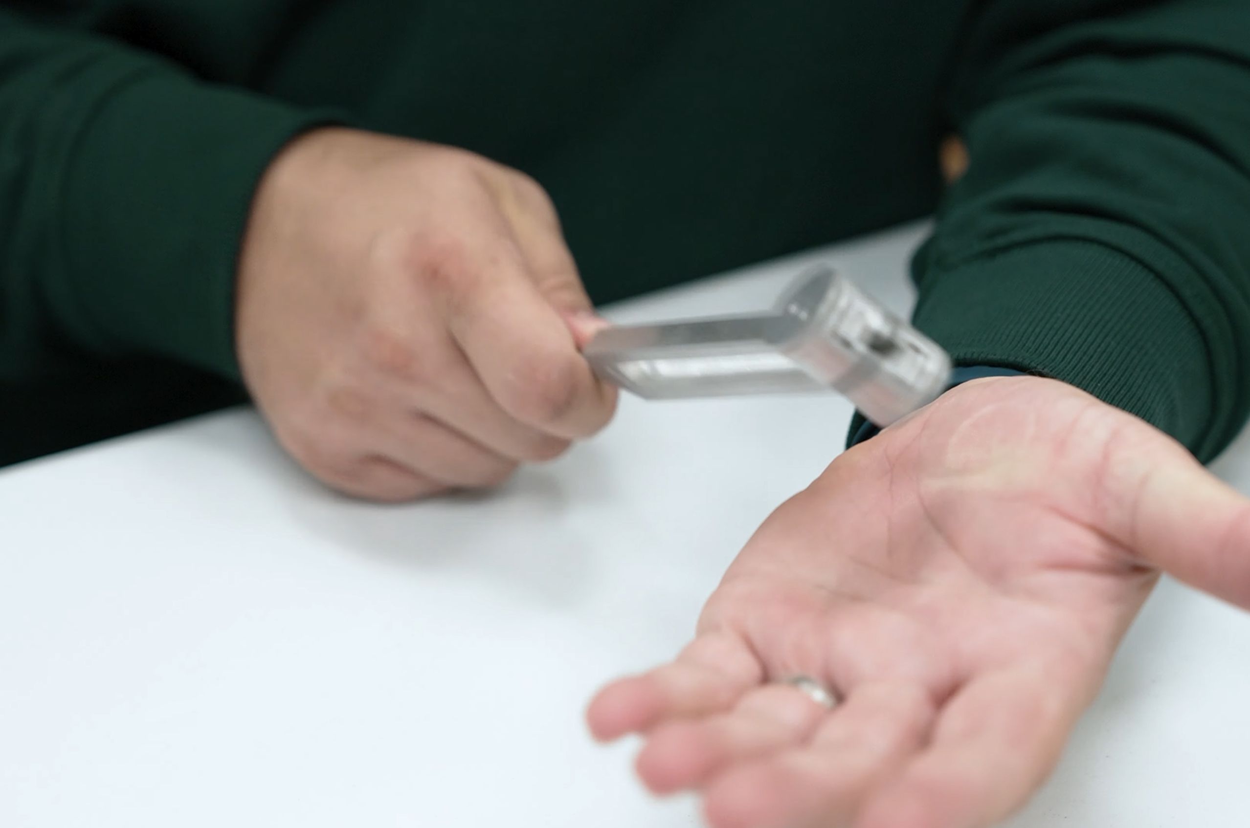 A person in a green sweater holds a tuning fork over their palm, striking their hand.