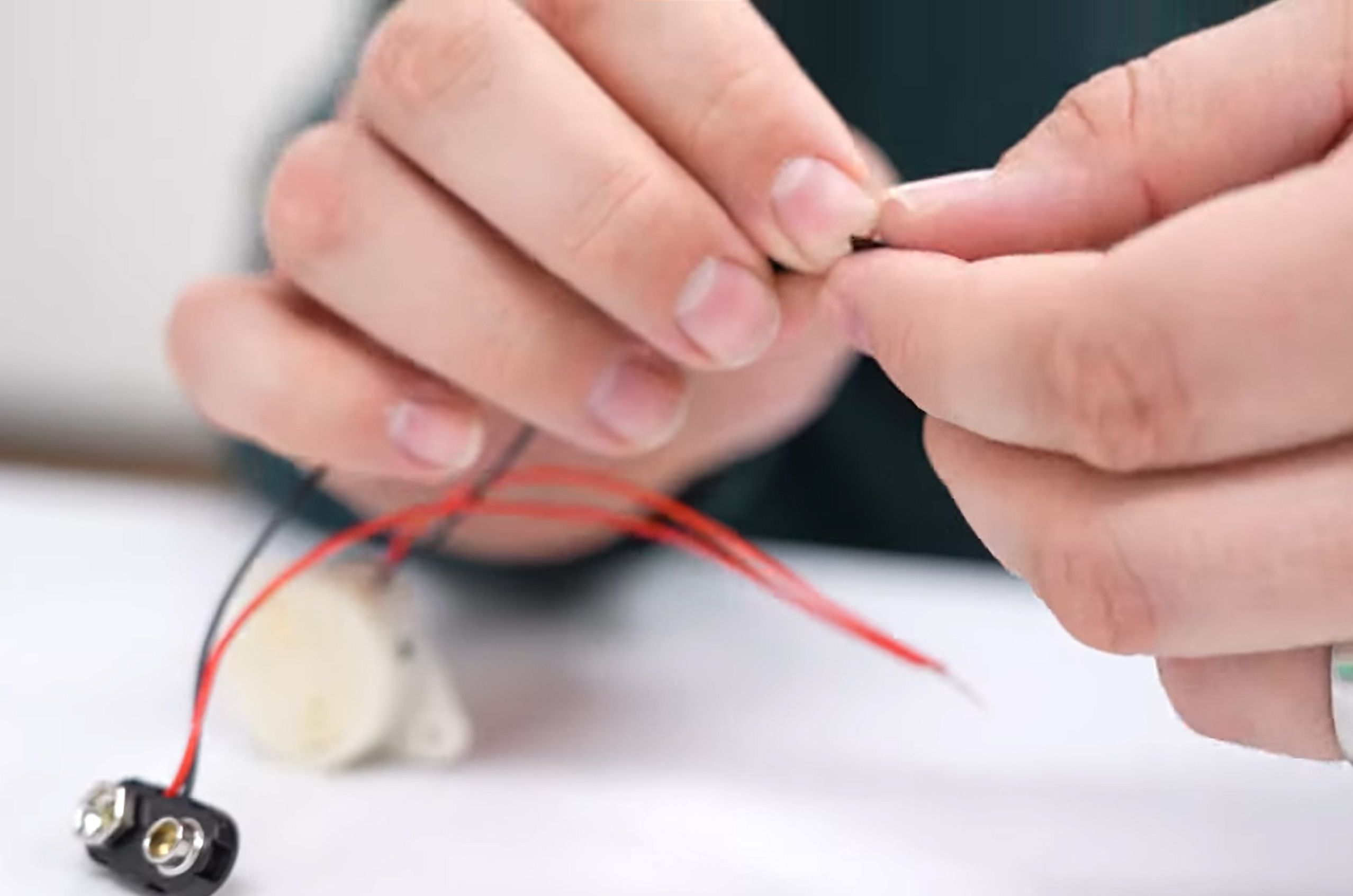 Hands connecting wires to a small electronic component on a white surface.