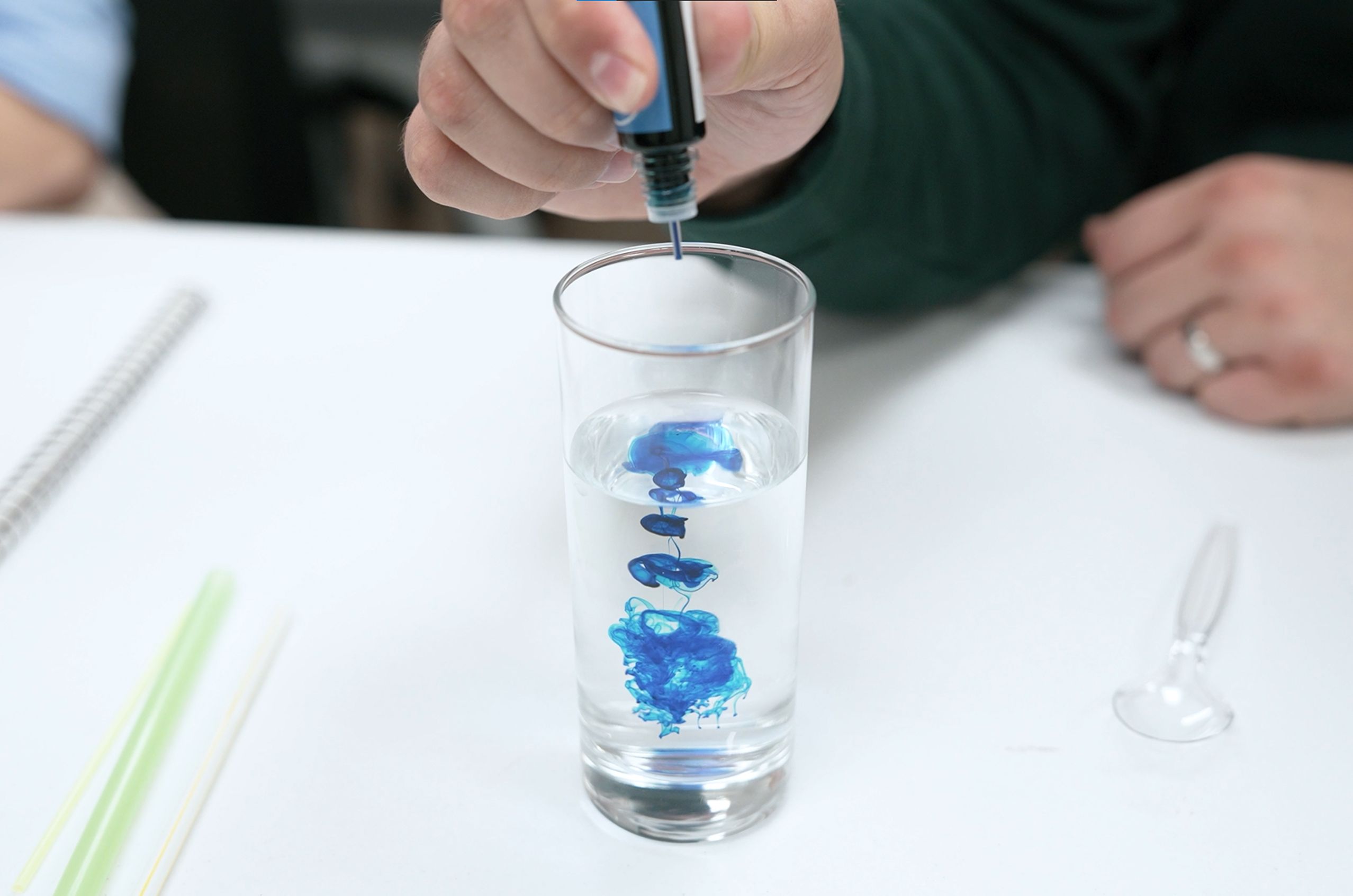 Hand dropping blue ink into a clear glass of water, creating swirling patterns.