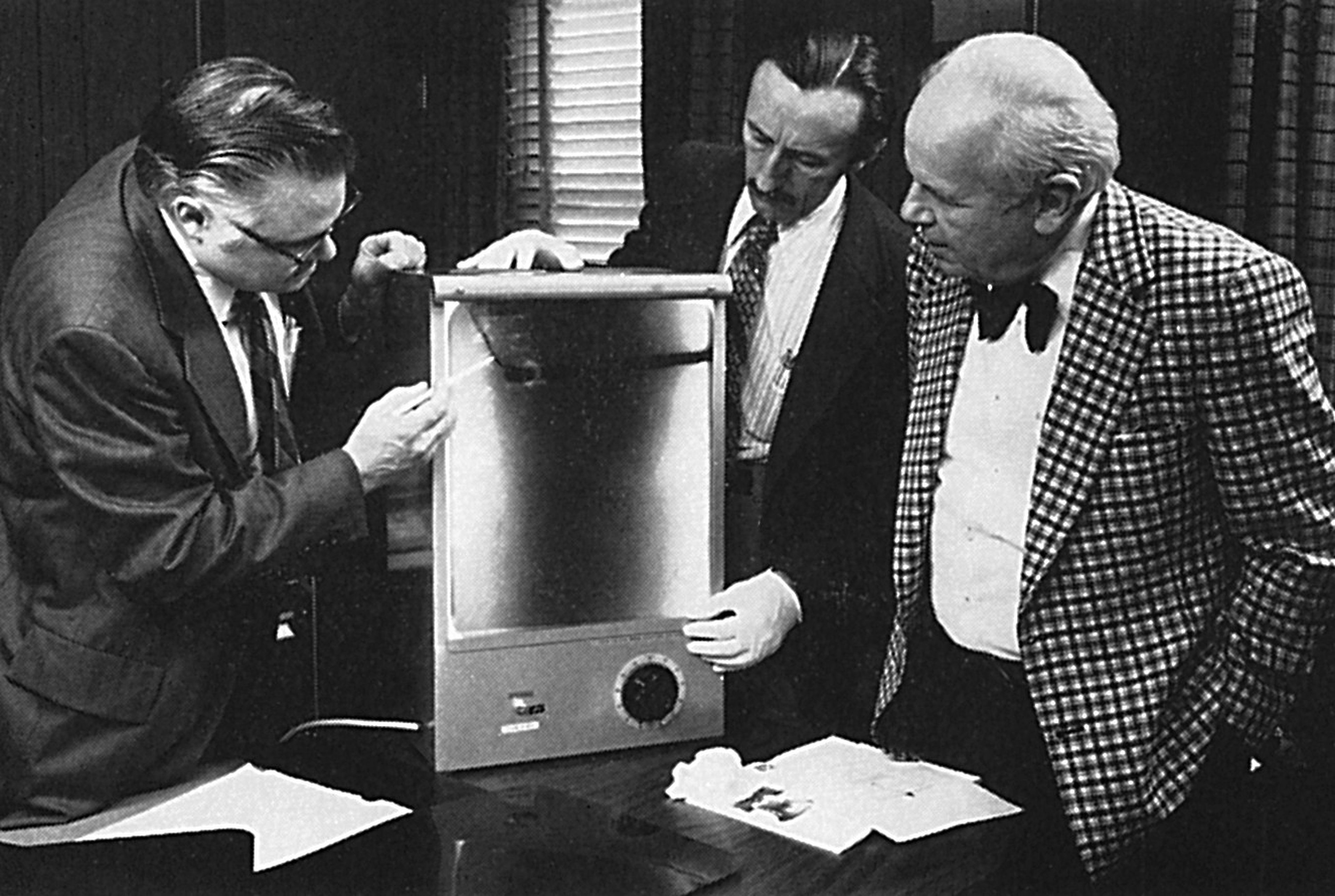 Vintage black-and-white photograph of NDT pioneers examining radiographs on a viewing device.