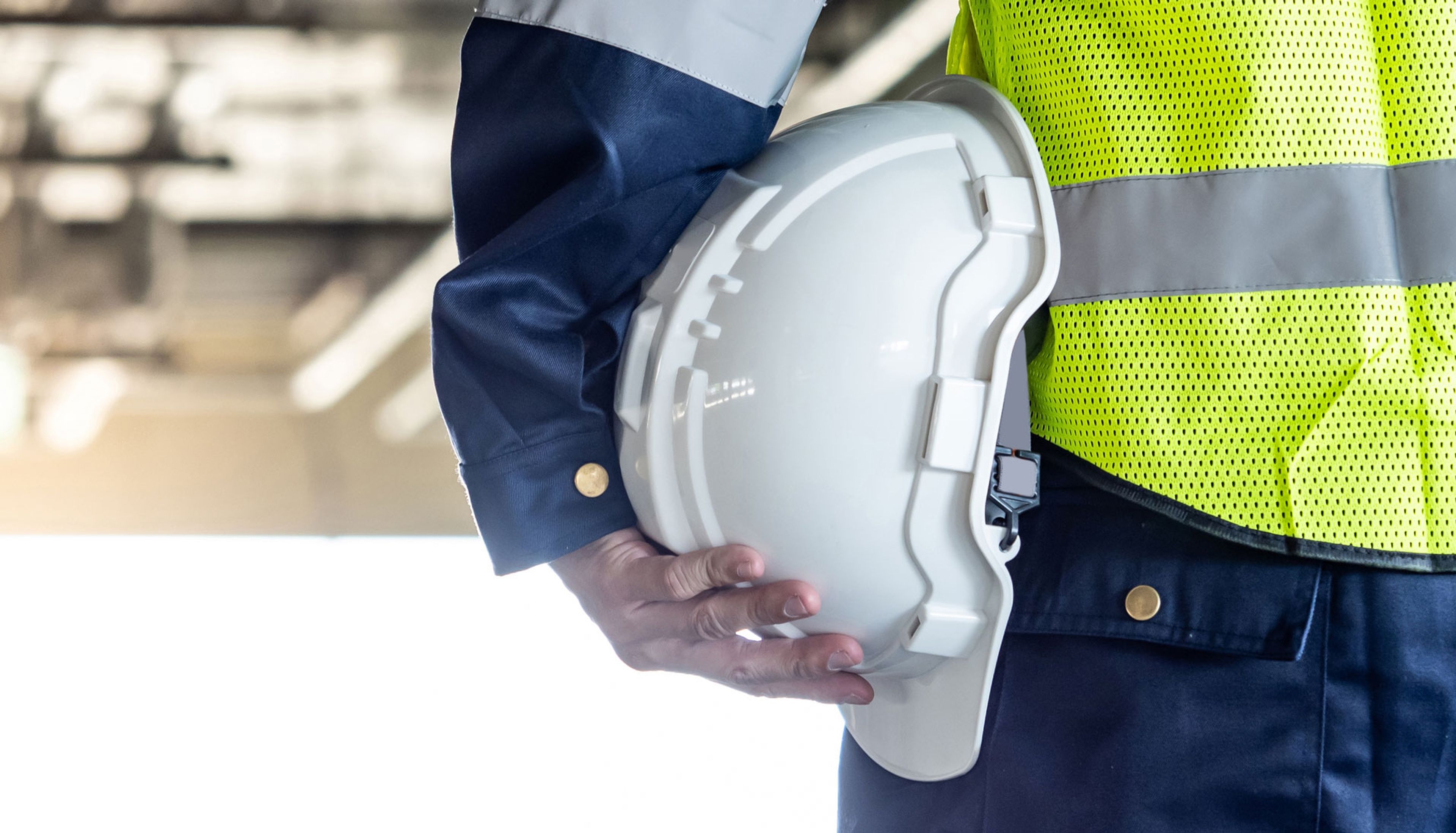 Safety worker in hi-vis vest holding a white hard hat