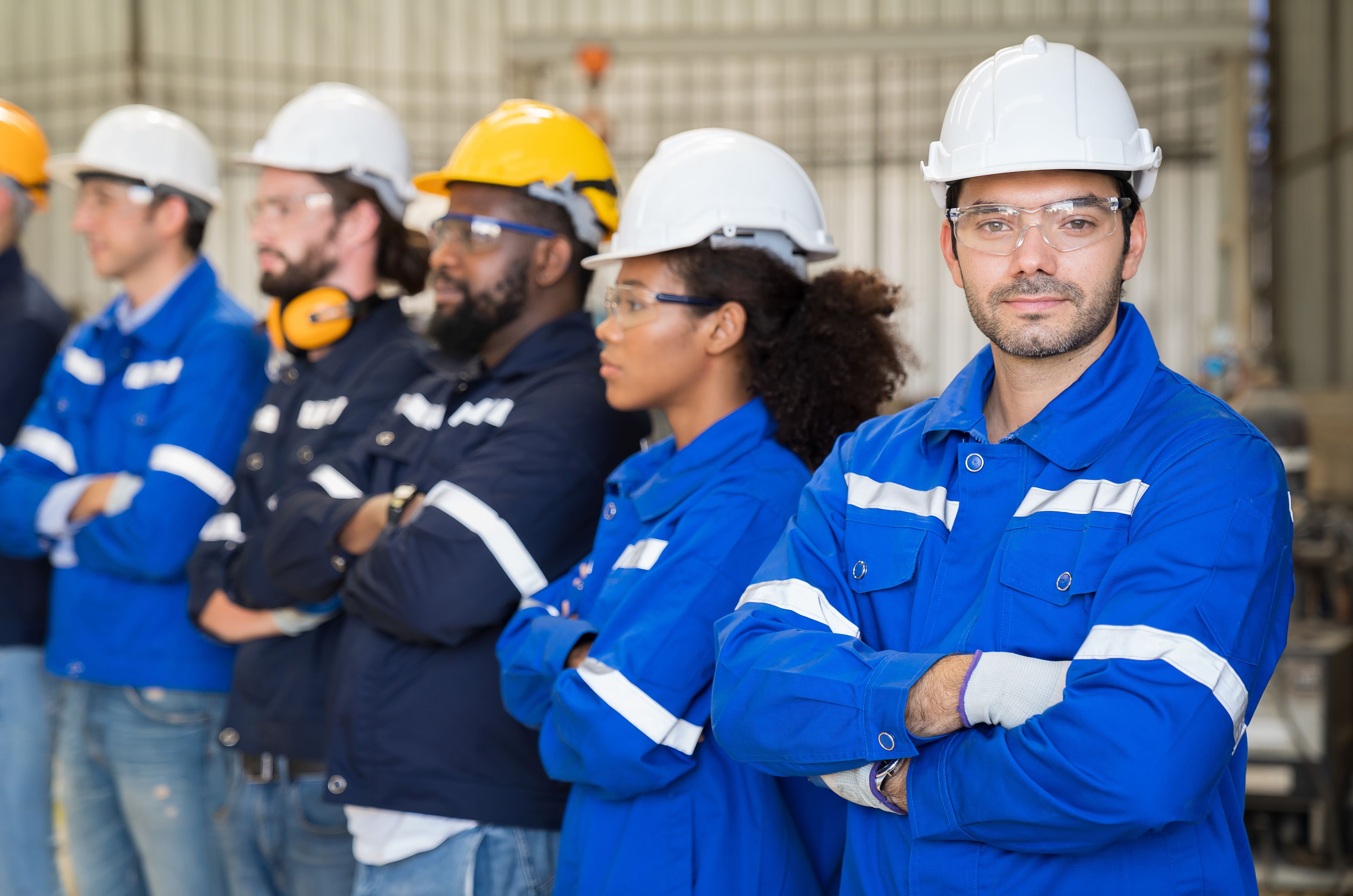 Group of industrial workers in blue uniforms and protective gear, standing with arms crossed, looking forward.