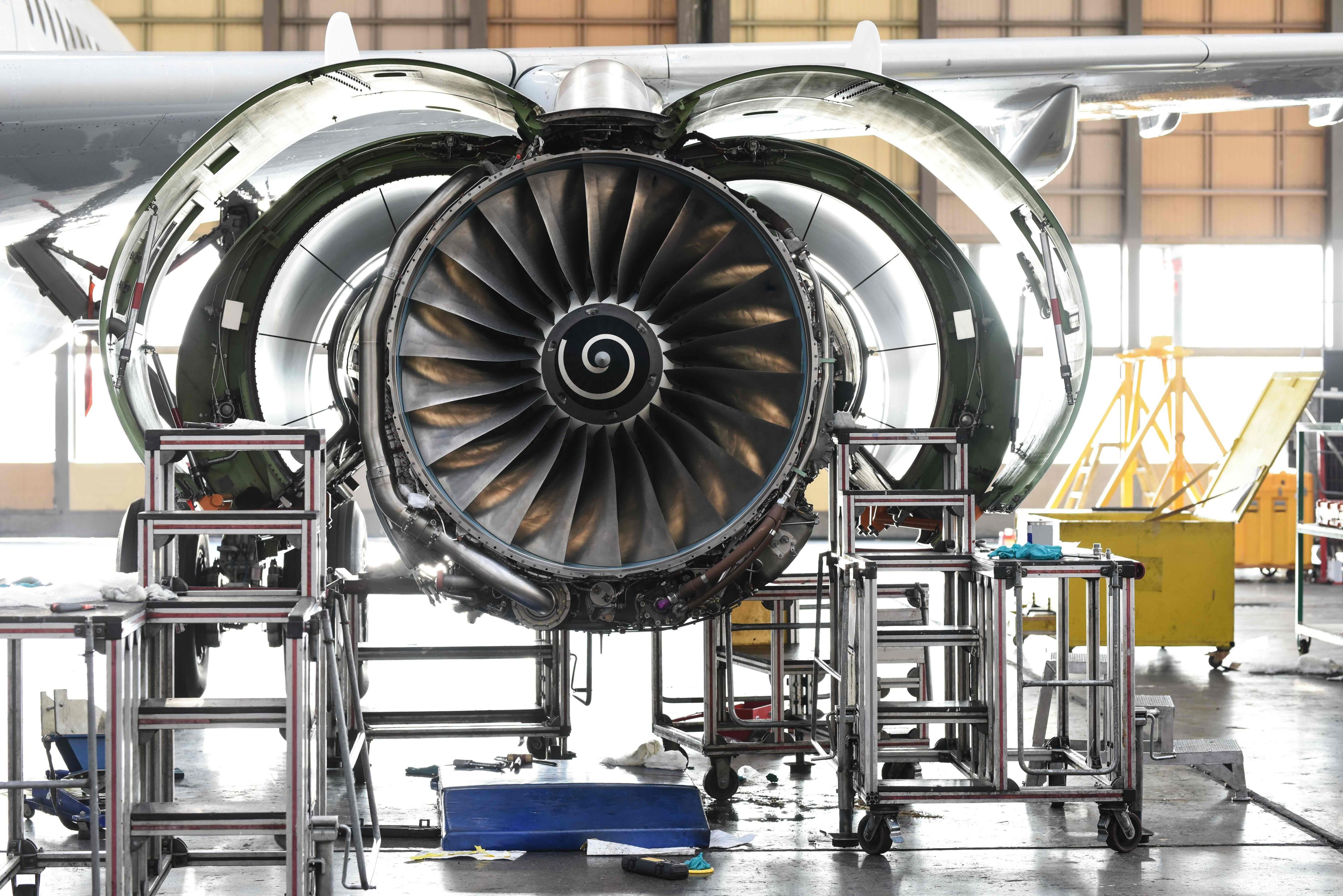 Aircraft engine undergoing maintenance in a hangar, with open cowling and various tools and equipment surrounding it.