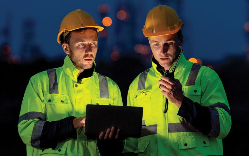 Two workers looking at a laptop, faces illuminated by laptop light.