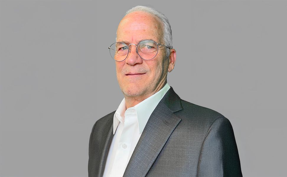 Dwight Witter, wearing a gray suit and white shirt, smiling against a plain gray background.