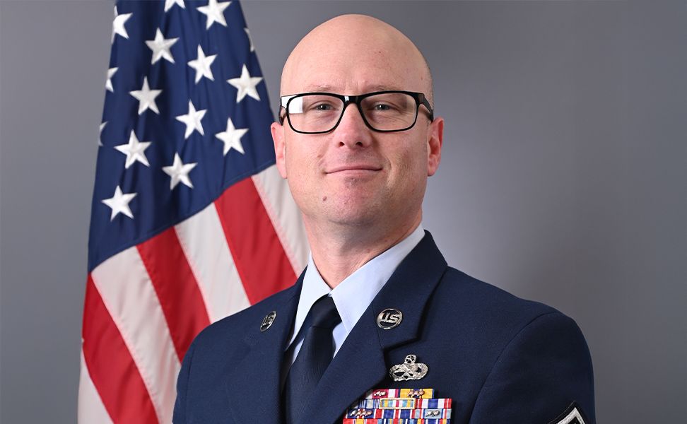 Matthew Baker in front of the American flag, wearing medals on their chest, looking confidently at the camera.