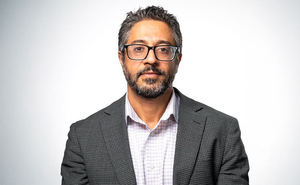 Ehsan Dehgan-Niri wearing a gray checkered suit and white collared shirt, against a plain white background.