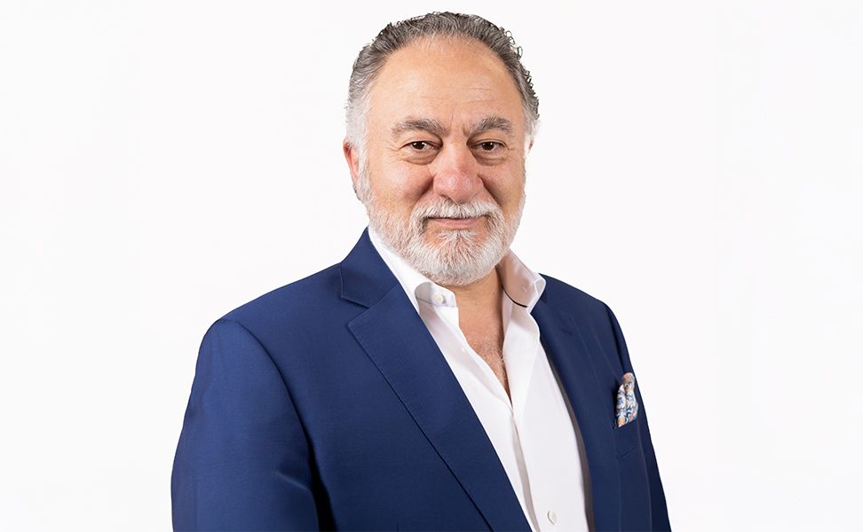 Shant Kenderian smiling, wearing a blue suit and white shirt, against a white background.