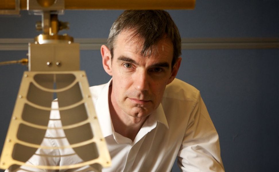 Tiny Peyton in a white shirt looking intently at a metallic structure in an office setting.