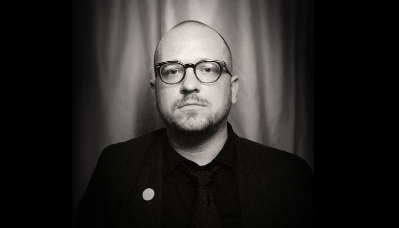 Black and white portrait of Tanner Woodford|Wills interviews Tanner with the back area of the Chicago Design Museum|Wills interviews Tanner with the back area of the Chicago Design Museum with downtown Chicago in background|Portrait image of Greg Wittstock holding up a turtle.|Justin sits down with Greg Wittstock