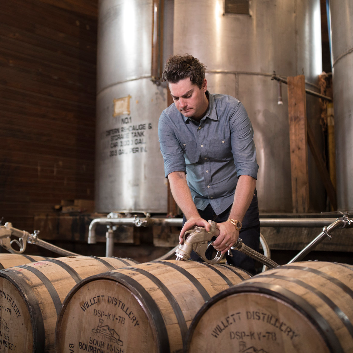Man filling wooden barrels with a hose in a distillery
