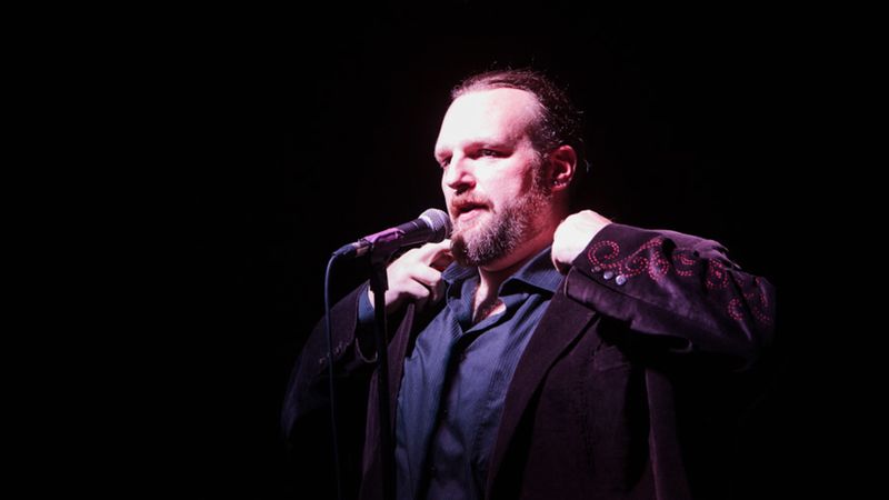 Peter Aguero talking into a microphone in a dark room
