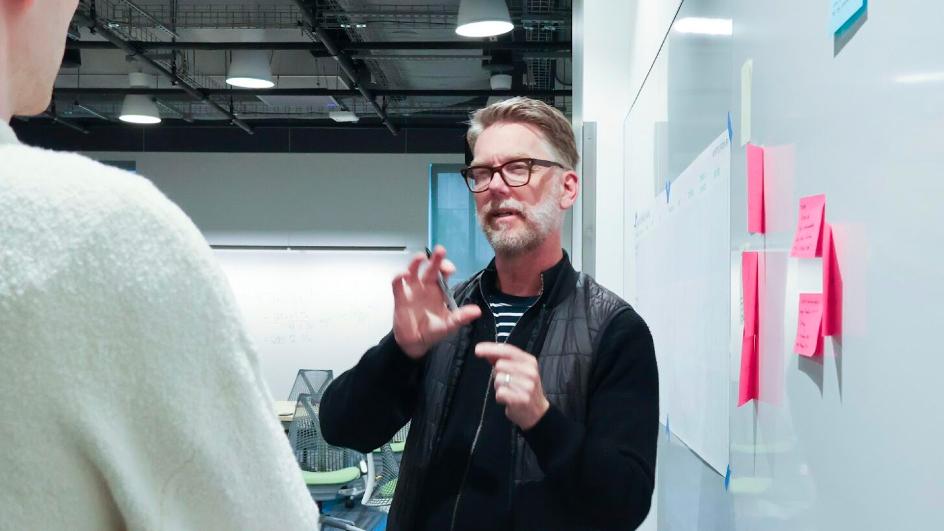 Doug-Powell explaining something to a person in front of a whiteboard with sticky notes on it