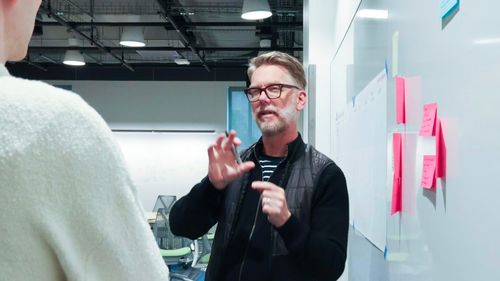 Doug-Powell explaining something to a person in front of a whiteboard with sticky notes on it