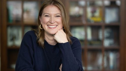 Sarah resting her chin on her hand in front of bookshelves blurred in the background