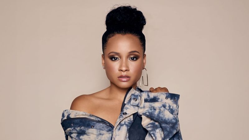 Rhyon Brown in a blue tie-dye jacket posing against a beige background.