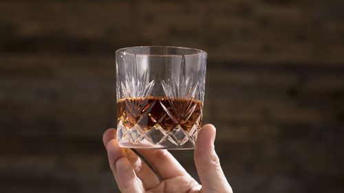 Hand holding up a crystal engraved glass with bourbon
