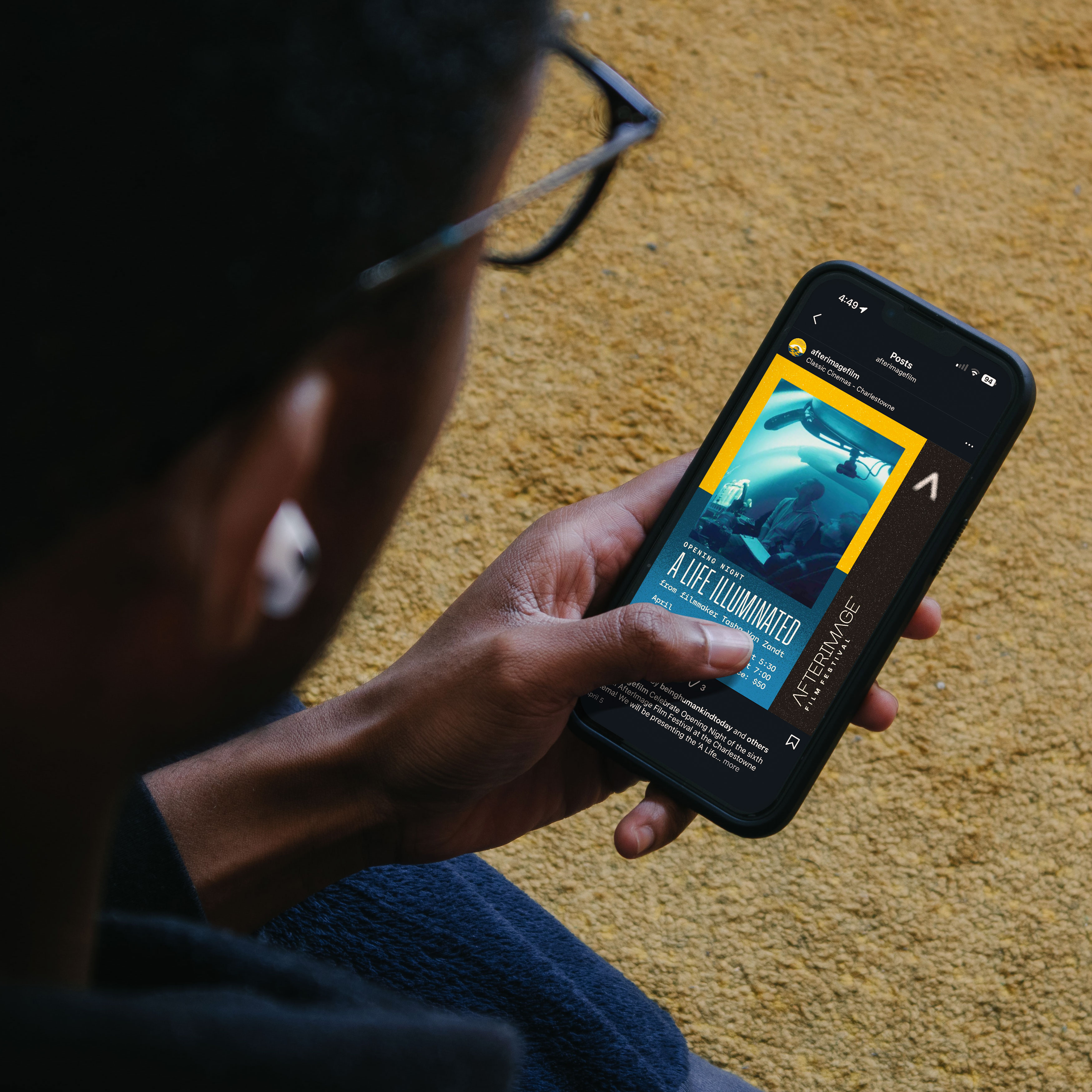 Person holding a phone displaying a social post promoting the 2026 AfterImage Film Festival