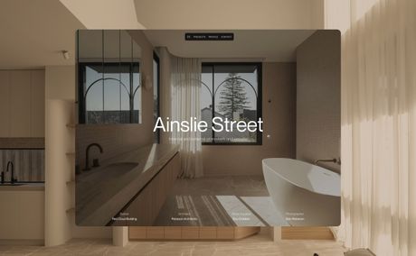 Modern bathroom with a freestanding tub, large window with a tree view, and subtle lighting. Project description overlay reads "Ainslie Street."