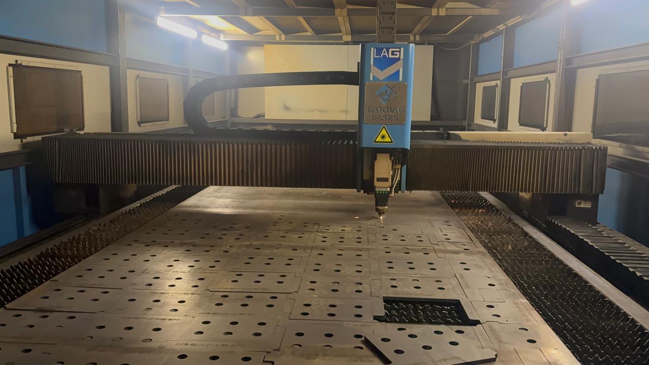 Máquina de corte a laser azul em oficina industrial, com chapa metálica posicionada e recortes precisos visíveis.