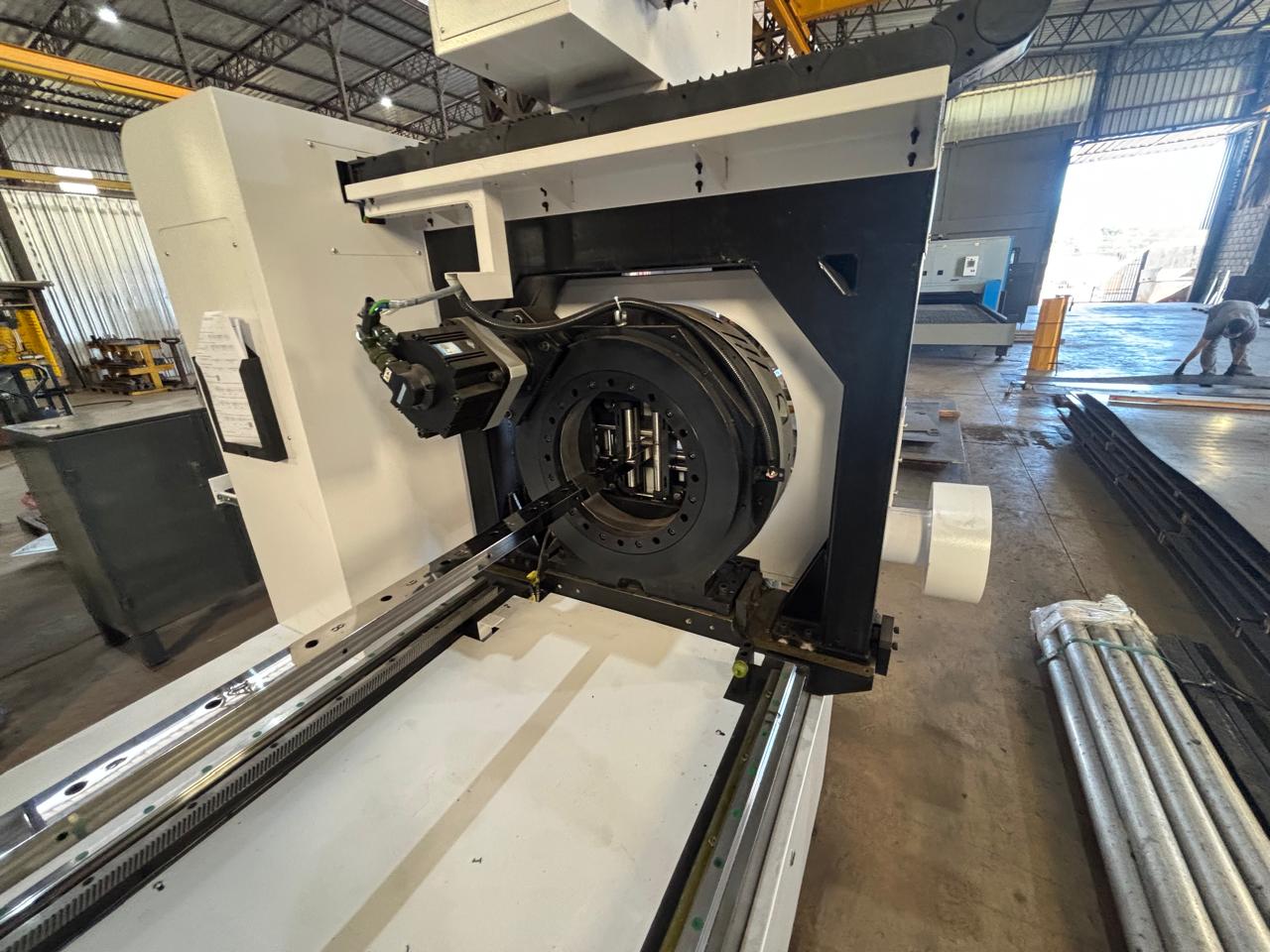 Máquina CNC industrial branca e preta em oficina, com componentes metálicos e trilho de guia horizontal.