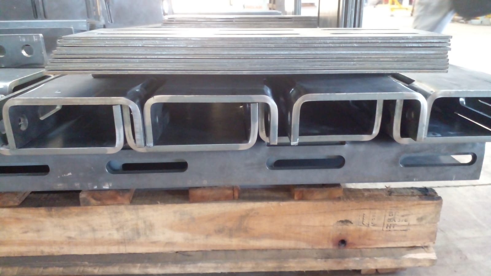 Palete com perfis metálicos ocos e chapas empilhadas em oficina industrial, sobre piso de concreto.