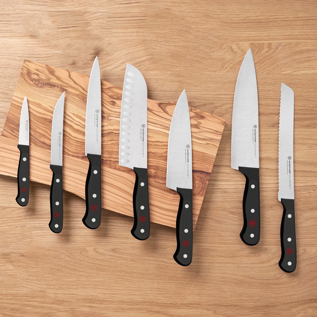 variety of black knives sitting overtop a wooden cutting board