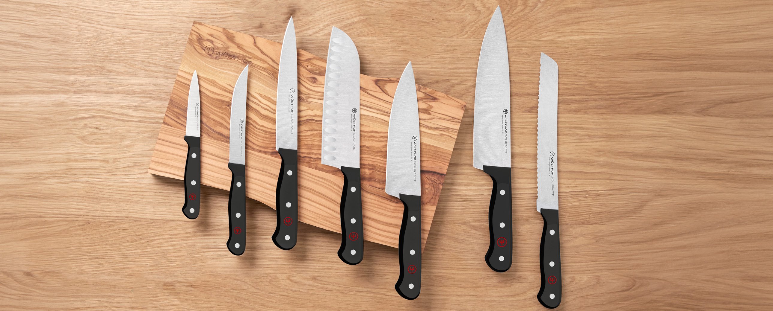 variety of black knives sitting overtop a wooden cutting board