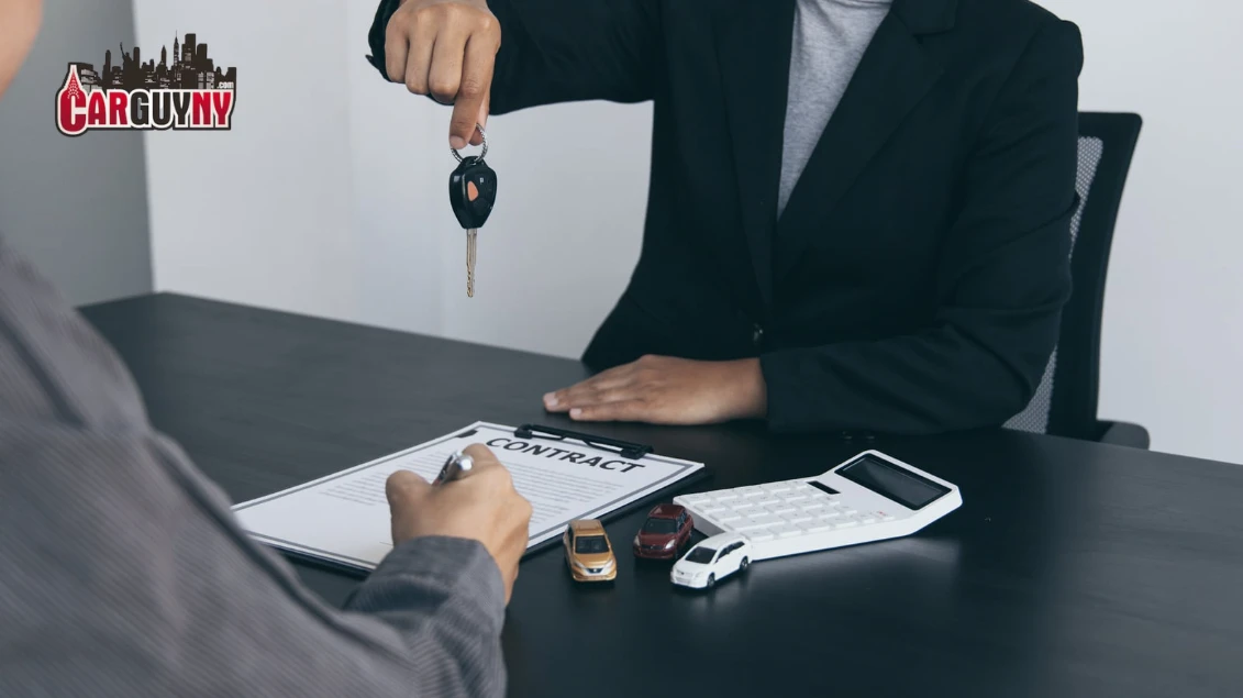 Person signing a car contract at a table with miniature cars, a calculator, and receiving car keys.