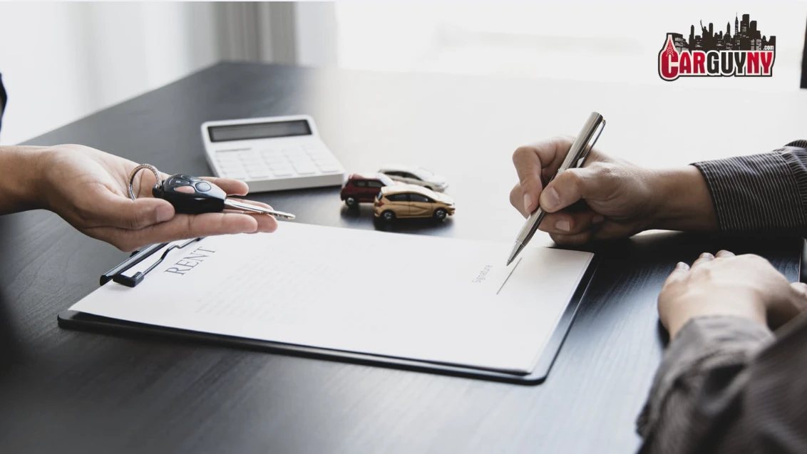 Person signing a car rental agreement at a desk with a set of car keys, toy cars, and a calculator nearby.
