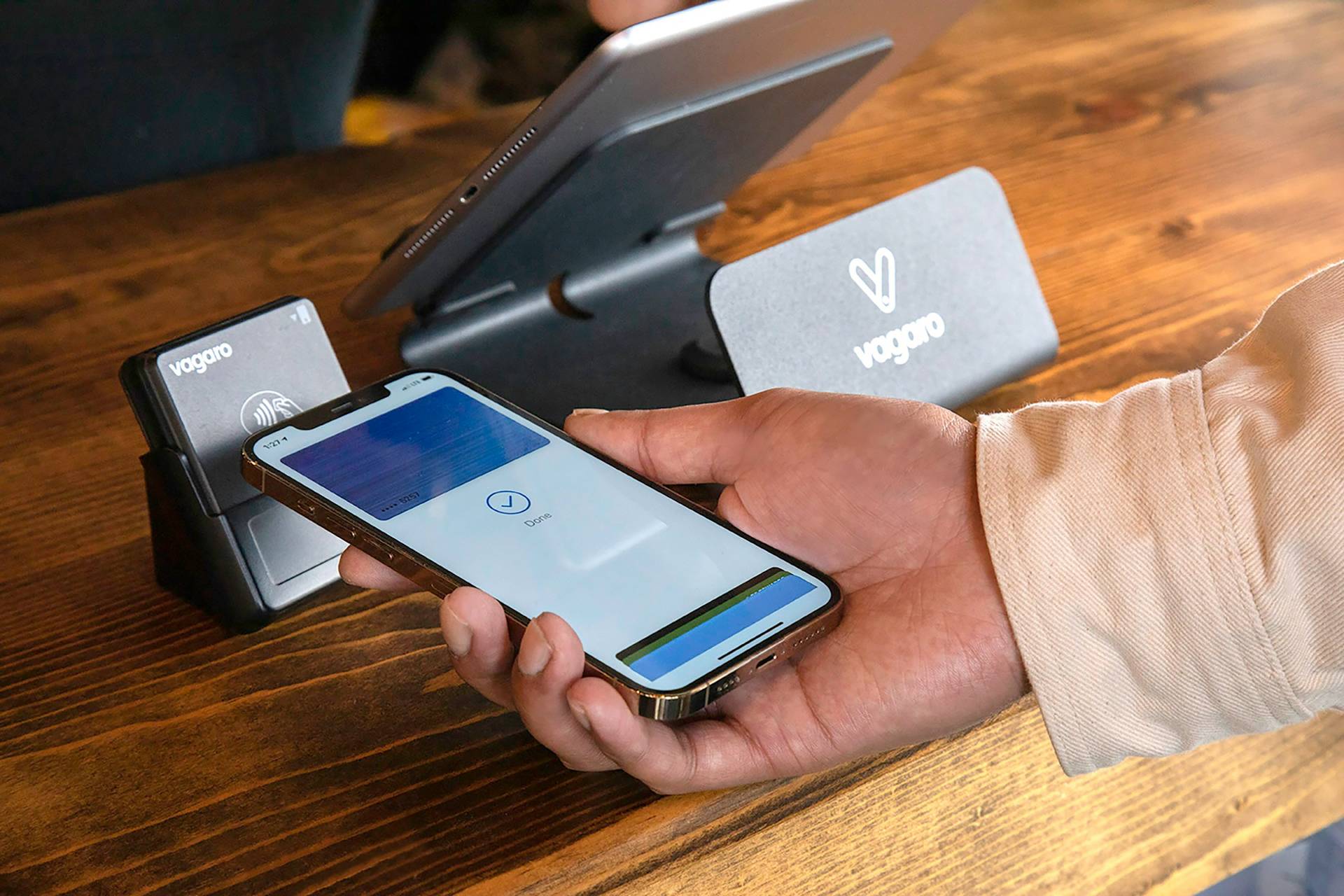 A person uses a smartphone for contactless payment at a point-of-sale terminal on a wooden counter.