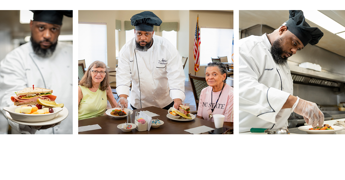 A chef in a kitchen serves food to two women at a table and prepares a dish, showcasing a sandwich and fruit on the plates.
