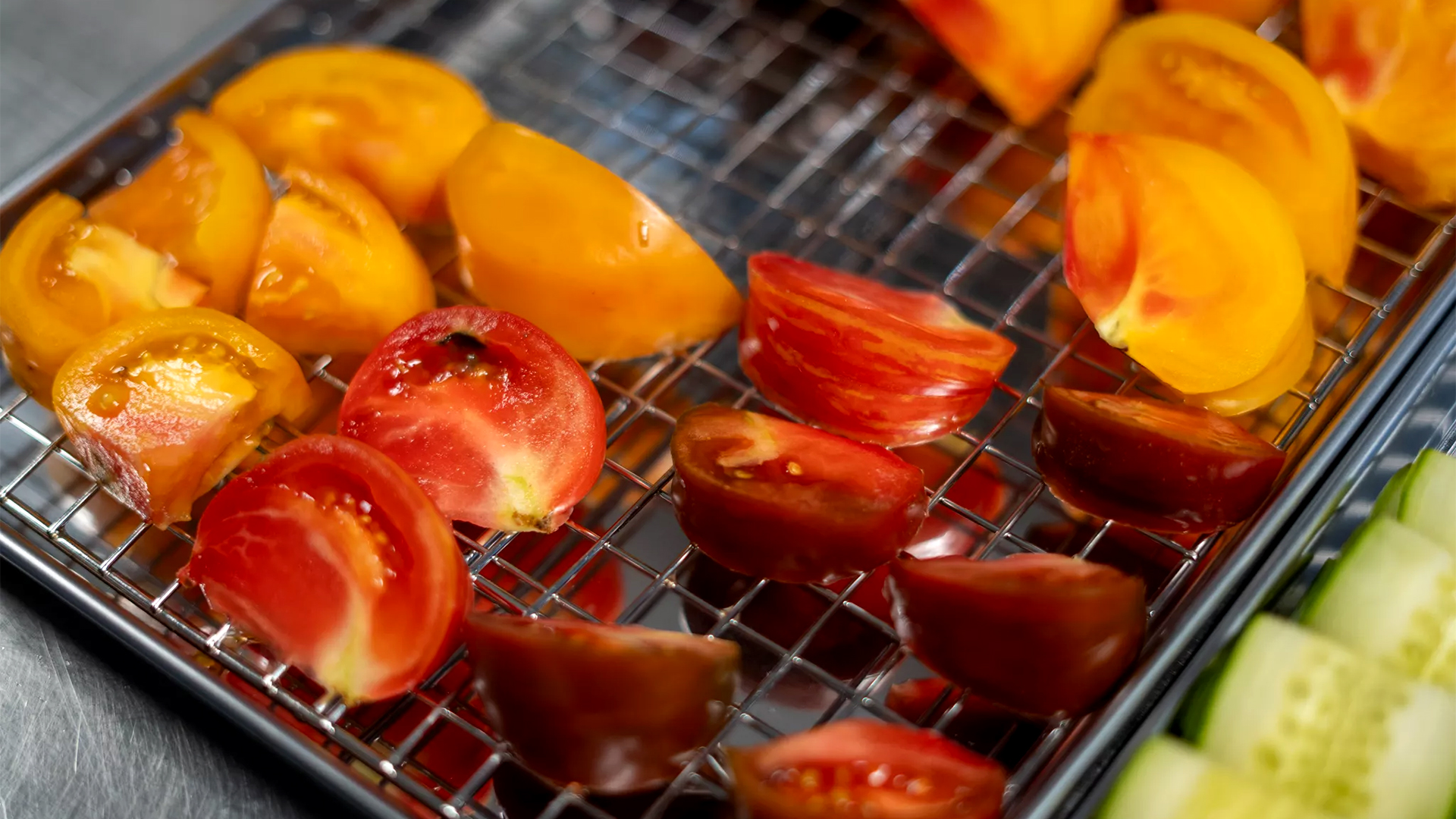Sliced red and yellow tomatoes on a wire rack, with cucumber slices visible at the edge.