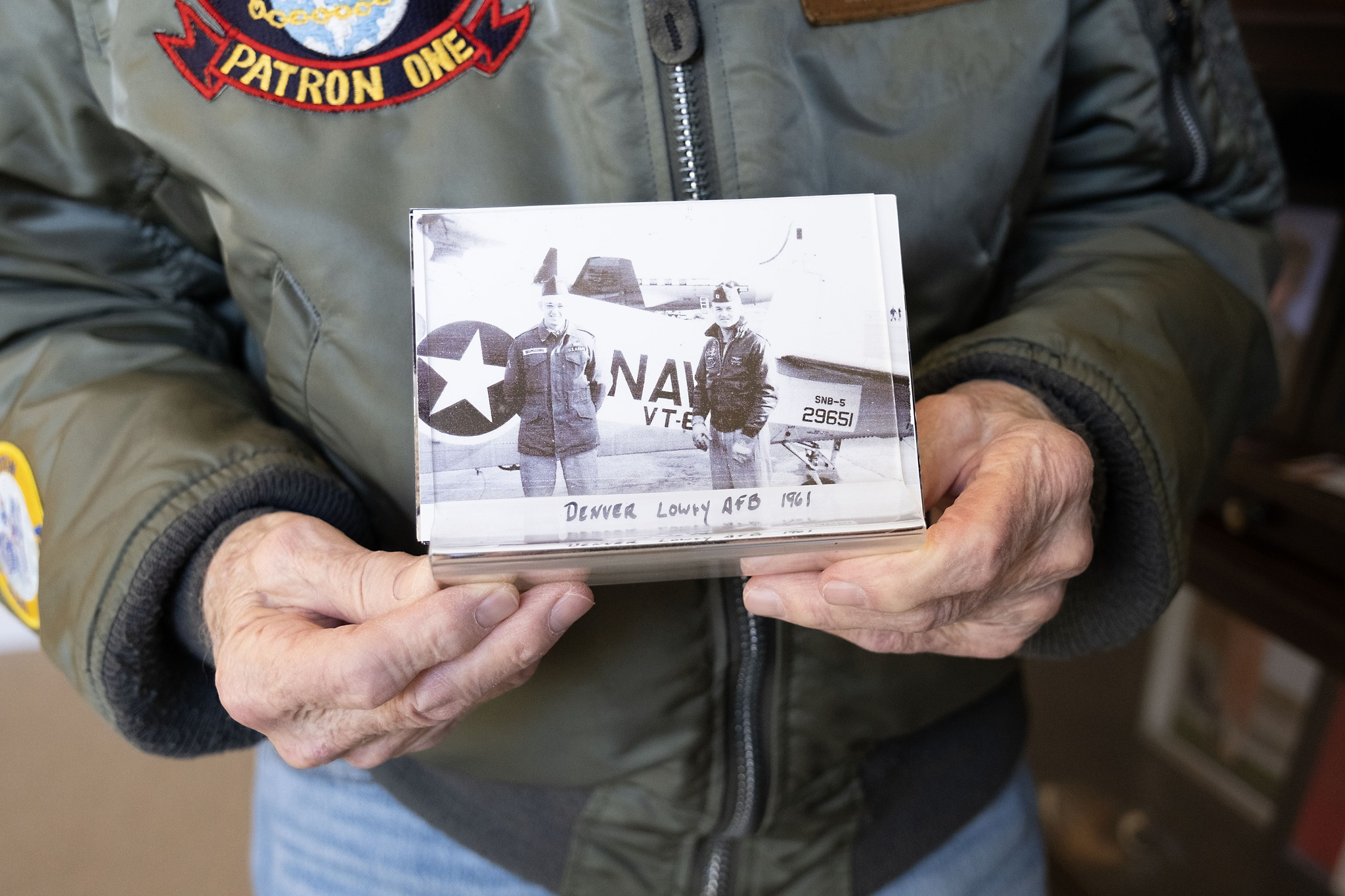 A person holding a vintage photo of two individuals in military attire in front of a plane, labeled 
