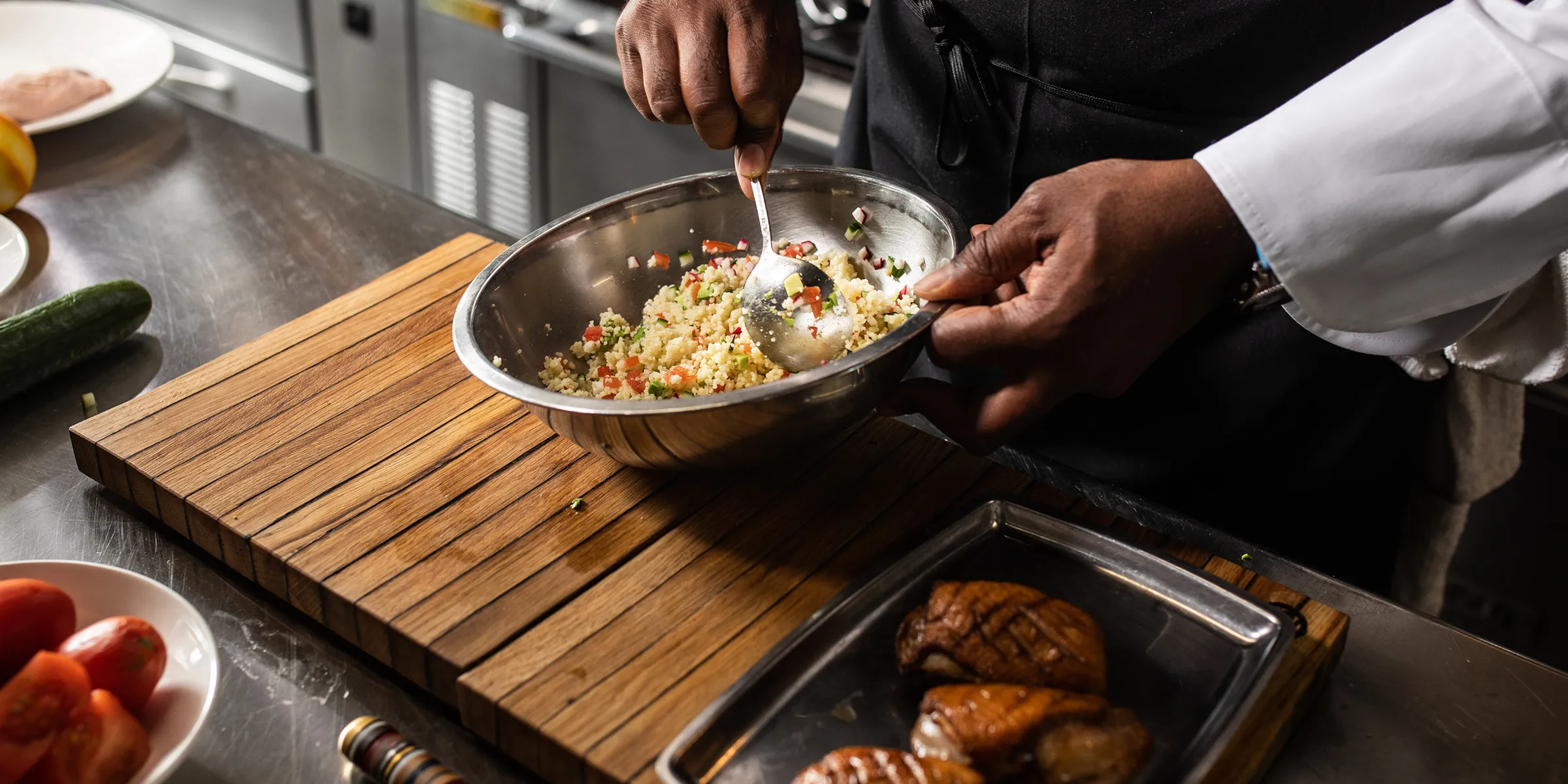 Chef mixing quinoa salad with metal spoon in metal bowl while standing in kitchen