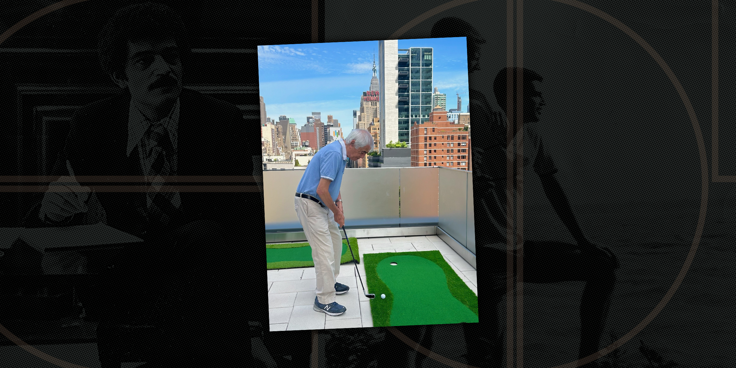 An older man plays mini golf on a rooftop putting green with a city skyline in the background. He stands focused over a golf ball, holding a putter. Tall buildings and a bright blue sky frame the scene.