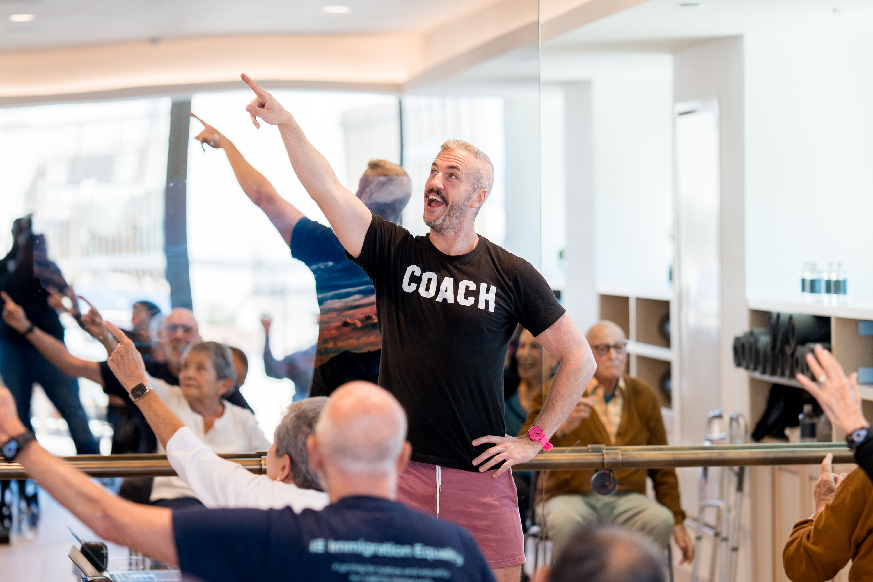 A group of people in a room mirrors a coach in a black 