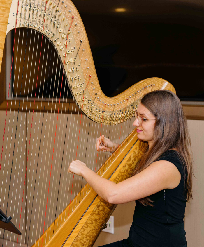 Female musician wearing a black dress and glasses playing large golden cello