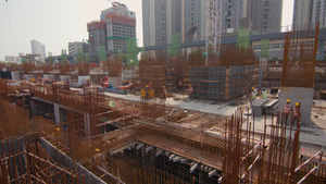 Construction site with steel frameworks and cranes, workers in helmets, and high-rise buildings in the background under a clear sky.