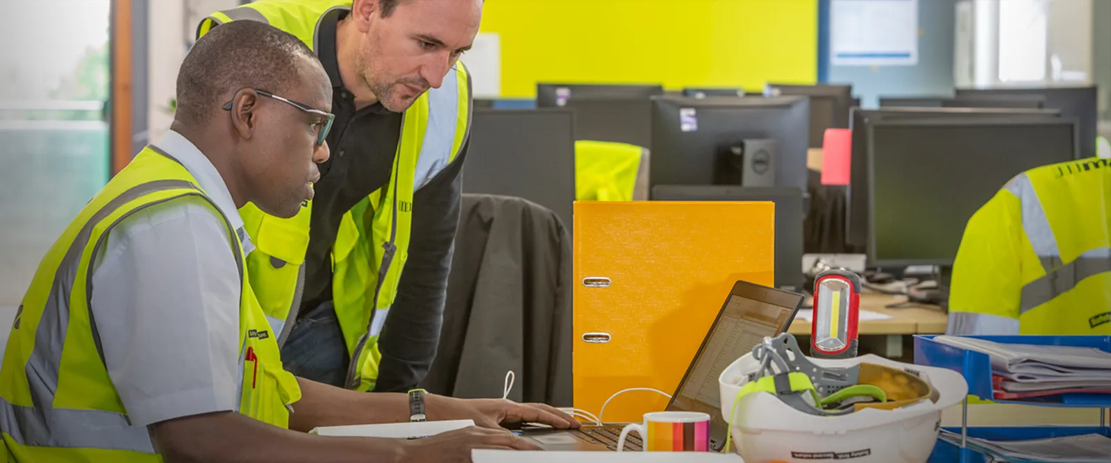 Two members of construction team looking at a laptop to evaluate and improve construction cost management and control.